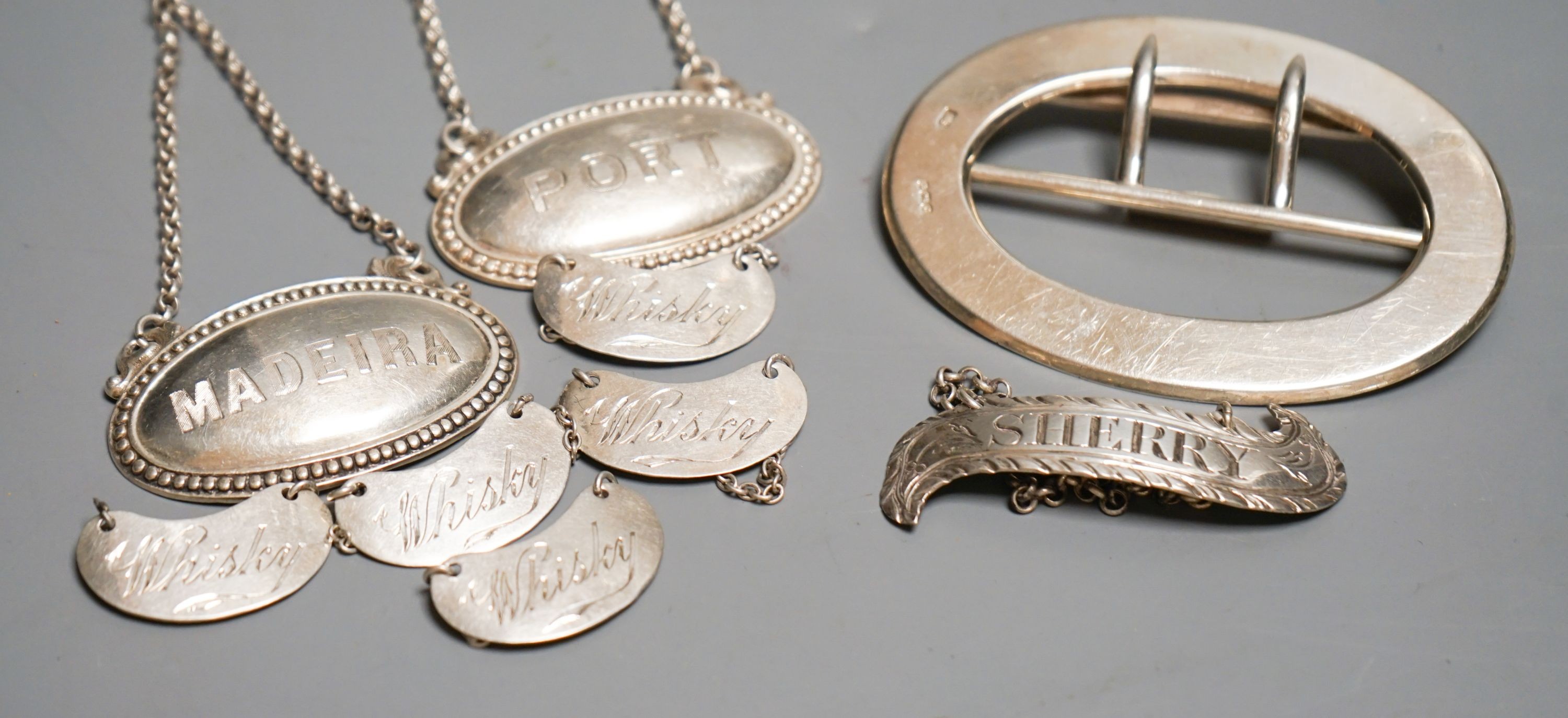 Eight assorted mainly 20th century silver wine labels and a n Edwardian silver belt buckle, 98 grams.